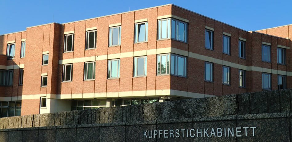 "KUPFERSTICHKA" 가 부분적으로 보이는 콘크리트 구조물 위에 여러 개의 창문이 있는 벽돌 건물. 맑고 푸른 하늘.