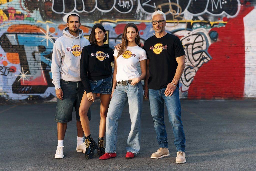 화려한 색상의 그래피티로 덮인 벽 앞에서 하드록 카페 의류를 입은 네 명이 포즈를 취하고 있습니다.