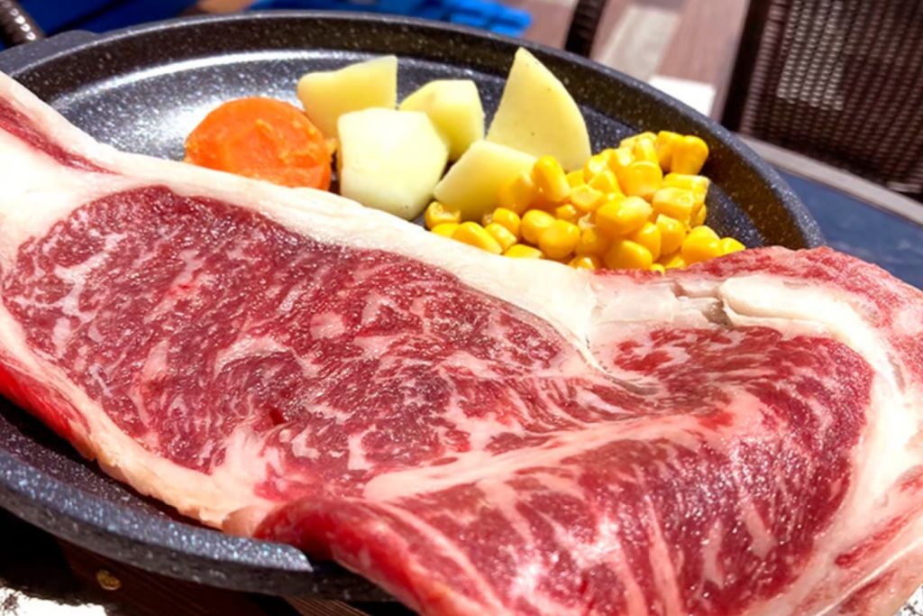 원시 구슬 쇠고기, 옥수수, 감자, 당근 한 조각이 담긴 접시가 테이블에 전시되어 있습니다.