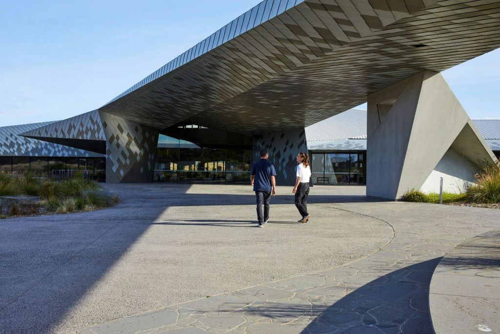 푸른 하늘 아래 각지고 반사되는 건축물이 있는 현대적인 건물을 향해 걸어가는 두 사람.