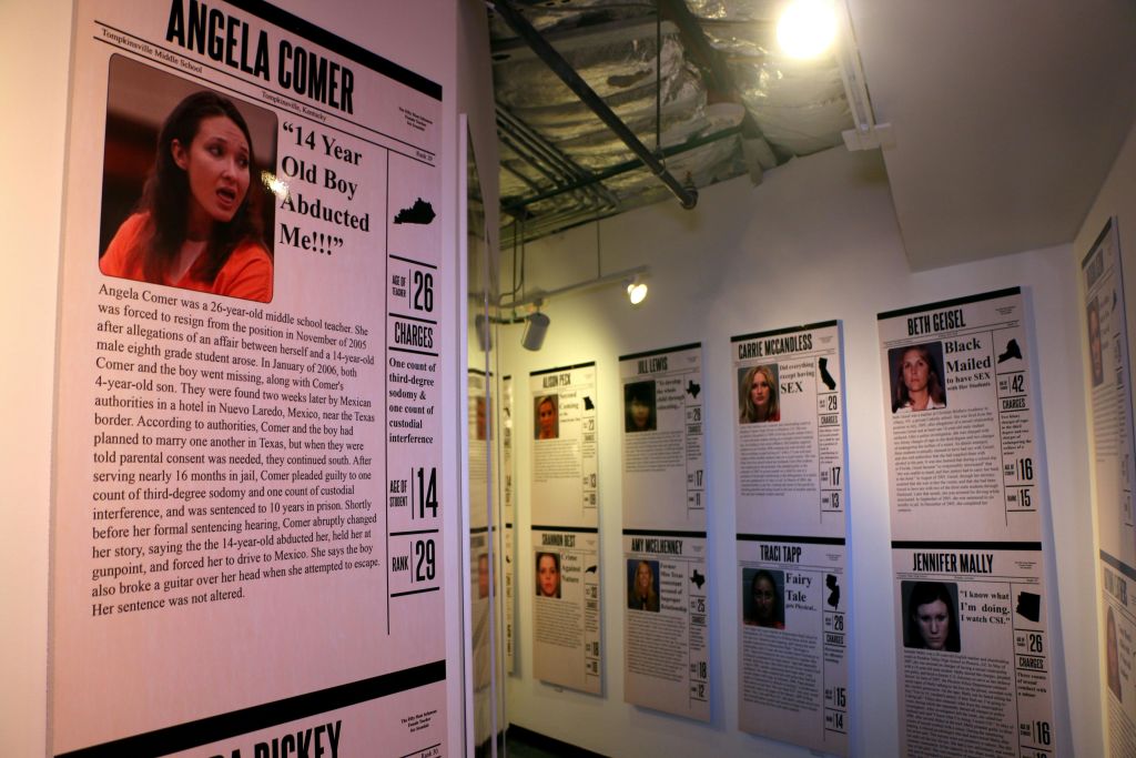 조명이 어두운 방에서 안젤라 코머 (Angela Comer) 와 다른 사람들에 대한 사진과 텍스트가 담긴 형사 사건에 대한 포스터가있는 벽을 전시하십시오.