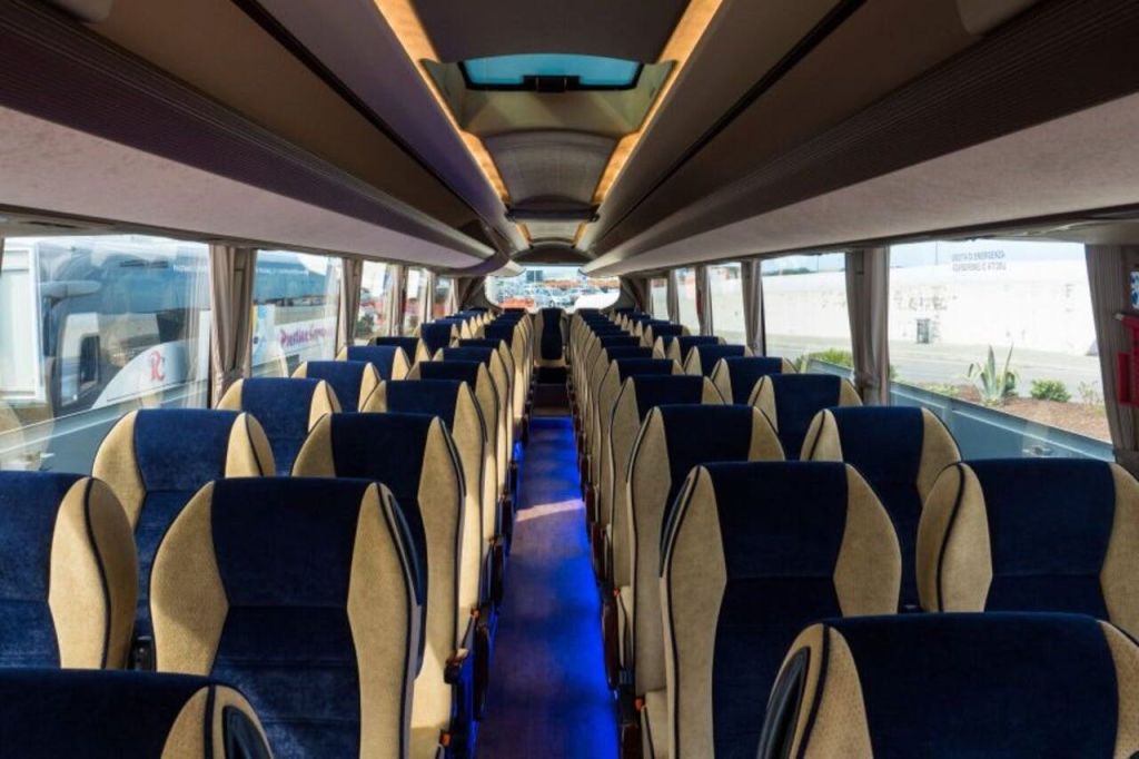 파란색과 베이지색 좌석이 줄지어 있는 현대적인 버스의 내부, 통로 조명, 양쪽에 커다란 창문이 있습니다.