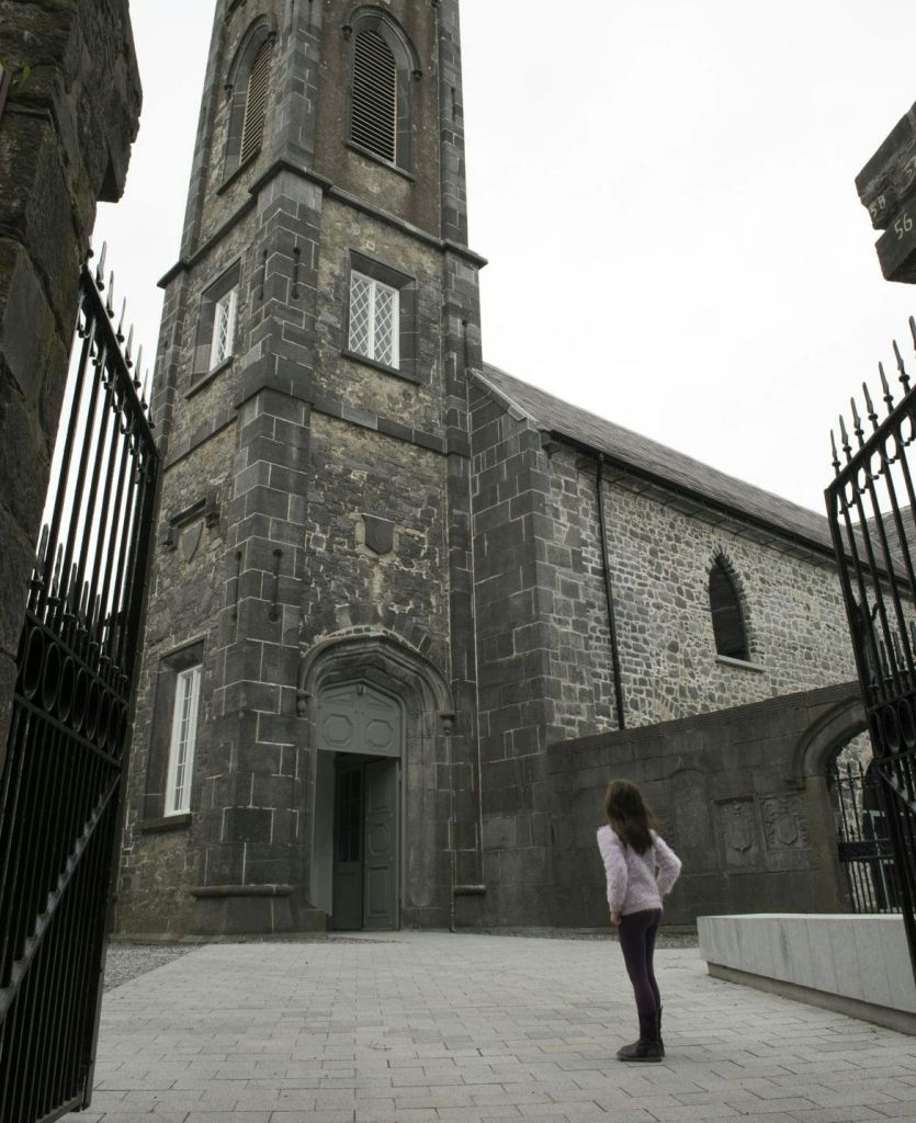 한 사람이 아치형 입구와 연철 문이 있는 역사적인 석조 교회 근처에 서서 건물을 올려다보고 있습니다.