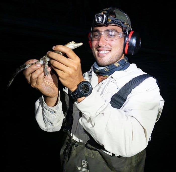 야외 장비와 전조등을 착용한 사람이 밤에 작은 파충류를 안고 미소를 짓고 있습니다.