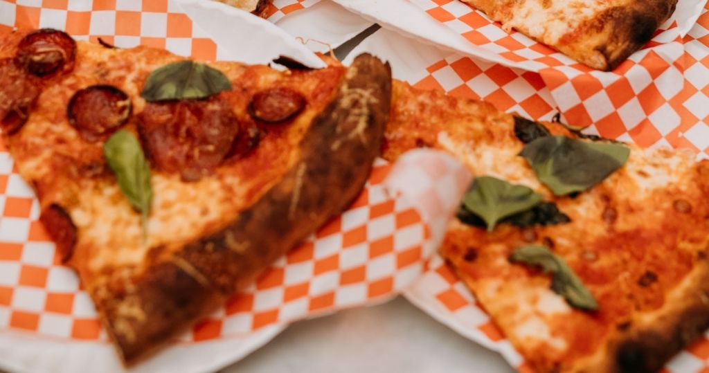 페퍼로니와 바질 같은 토핑이 들어간 피자 조각이 오렌지색과 흰색 체크무늬 종이에 놓여 있습니다.