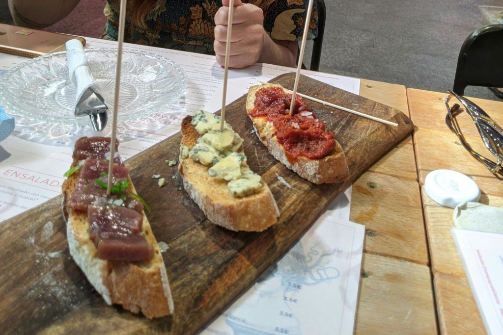 나무판에 다른 토핑을 얹은 빵 세 조각. 사람의 손이 배경에 보입니다.