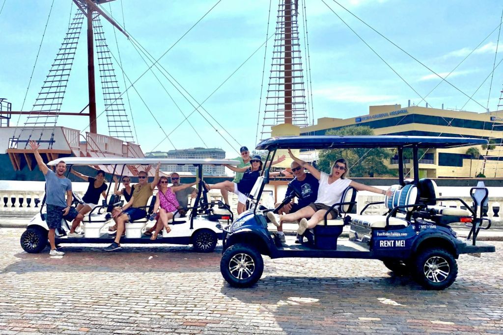 커다란 배를 배경으로 두 대의 렌트용 골프 카트 근처에서 한 무리의 사람들이 기분 좋게 포즈를 취하고 있습니다.