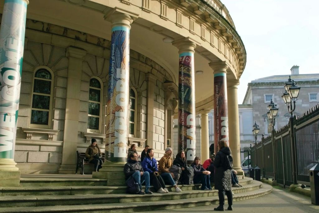 사람들은 "탐험", "읽기" 및 "배우기" 라는 단어가 표시된 커다란 기둥이있는 건물의 계단에 앉아서 이야기합니다.