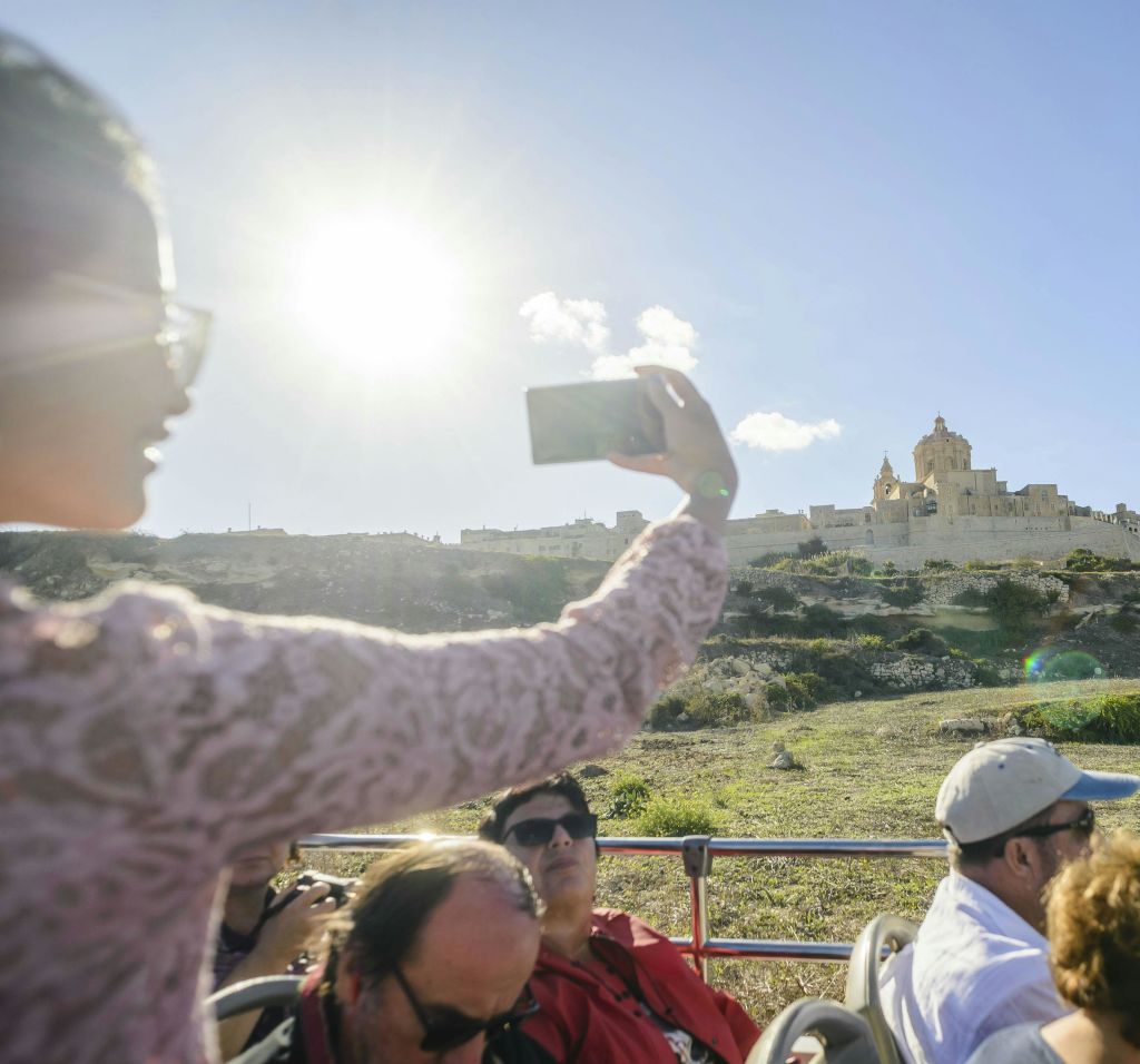 분홍색 레이스 상의를 입은 사람이 스마트폰으로 셀카를 찍고, 건물을 배경으로 아름다운 풍경을 감상합니다.