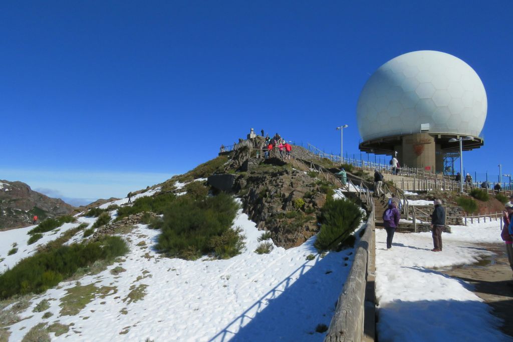 맑고 푸른 하늘 아래 눈 덮인 산봉우리의 커다란 구형 전망대를 향해 걸어가는 사람들.