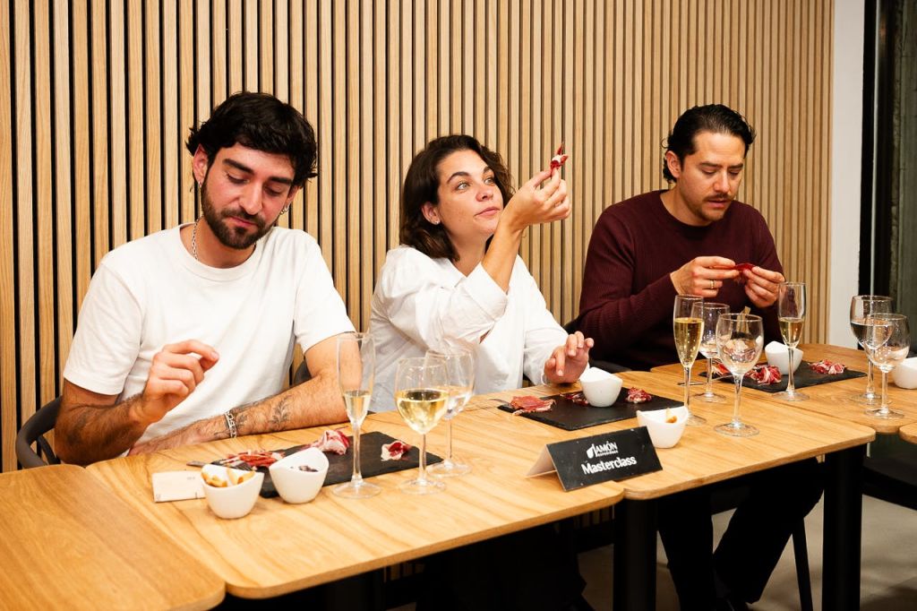 두 사람이 나무 테이블에 앉아 음식과 음료를 즐기고 있습니다. 한 명은 그들의 손을 관찰하고 다른 한 명은 작은 음식을 검사합니다.