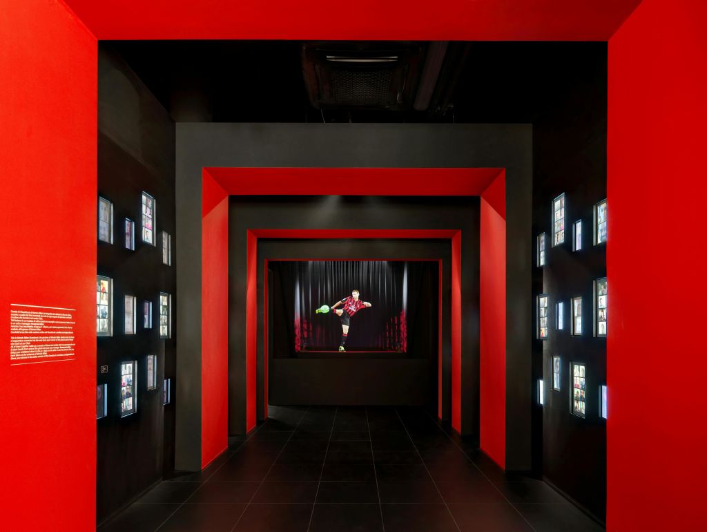 검은색 벽과 빨간색 프레임이 있는 복도에는 조명이 있는 작은 디스플레이가 있습니다. 마지막에는 무대에서 한 연주자가 팔짱을 낀 채 포즈를 취합니다.