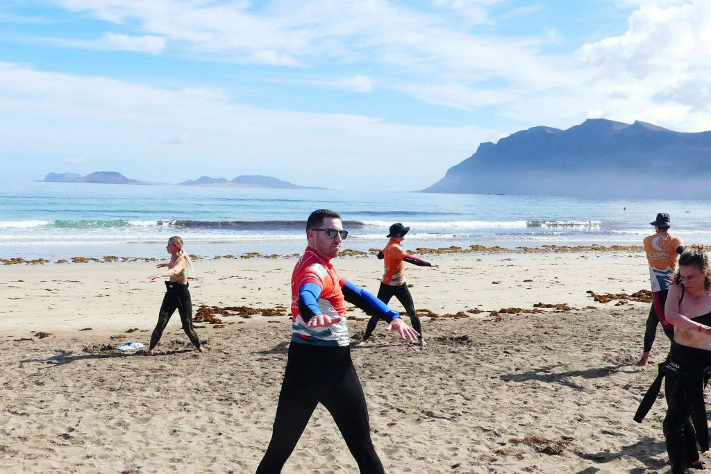 산과 바다를 배경으로 모래사장에서 운동복을 입은 세 사람.