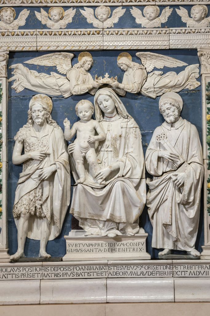 아이와 함께 앉은 마돈나를 포함한 종교적 인물을 묘사한 상세한 부조는 머리 위에 천사가있는 두 명의 성인이 측면에 있습니다.