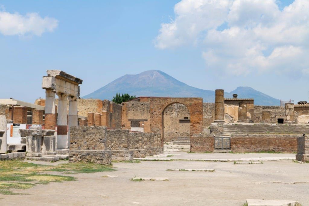 푸른 하늘 아래 석조 건물과 아치가 있는 고대 유적지. 저 멀리 산이 배경으로 보인다.