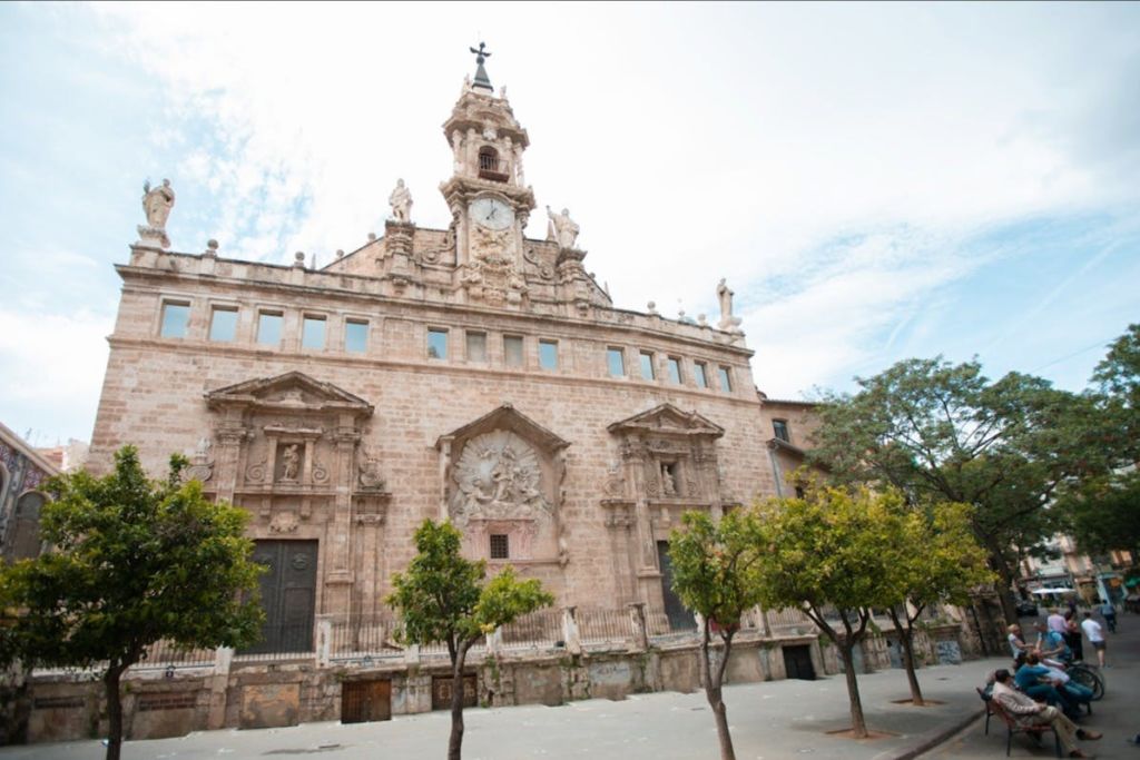 화려한 건축 디테일, 커다란 시계탑, 부분적으로 흐린 하늘 아래 전경의 나무가 있는 유서 깊은 석조 건물.