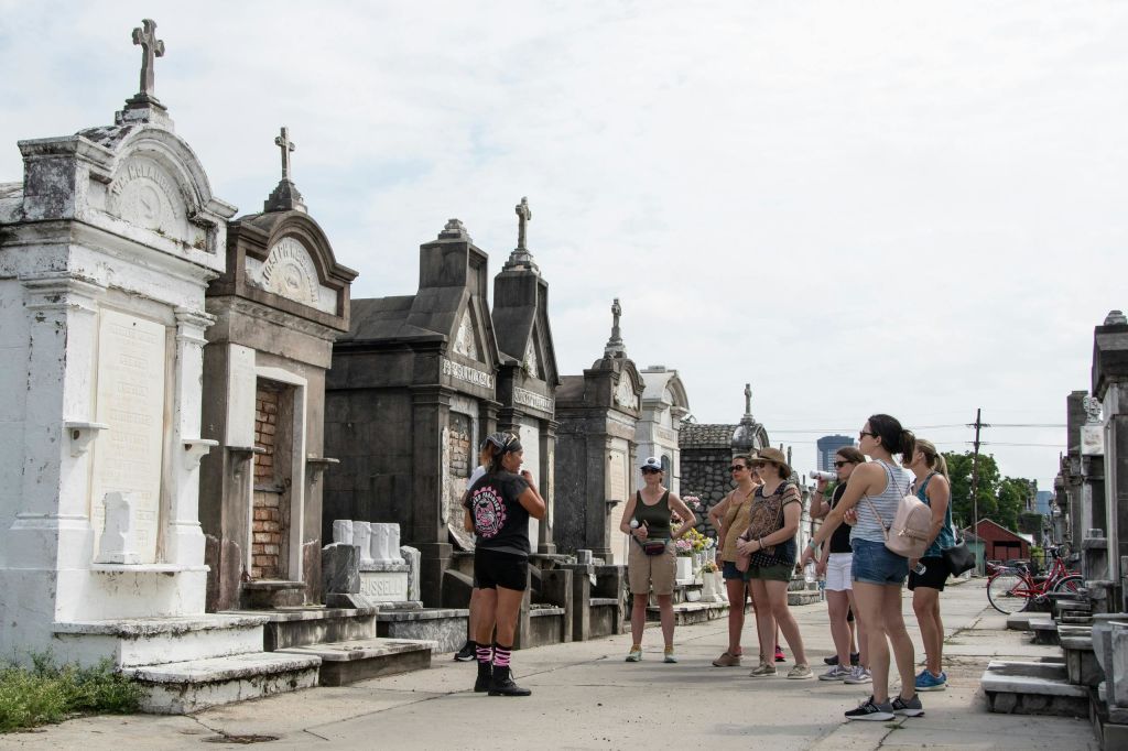 흐린 날, 지상 무덤이 있는 공동묘지에서 한 무리의 사람들과 이야기하는 투어 가이드.