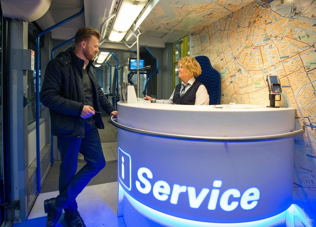 벽에 지도가 있는 현대적인 공간 내부의 조명 서비스 데스크에서 한 남성이 여성과 이야기를 나누고 있습니다.