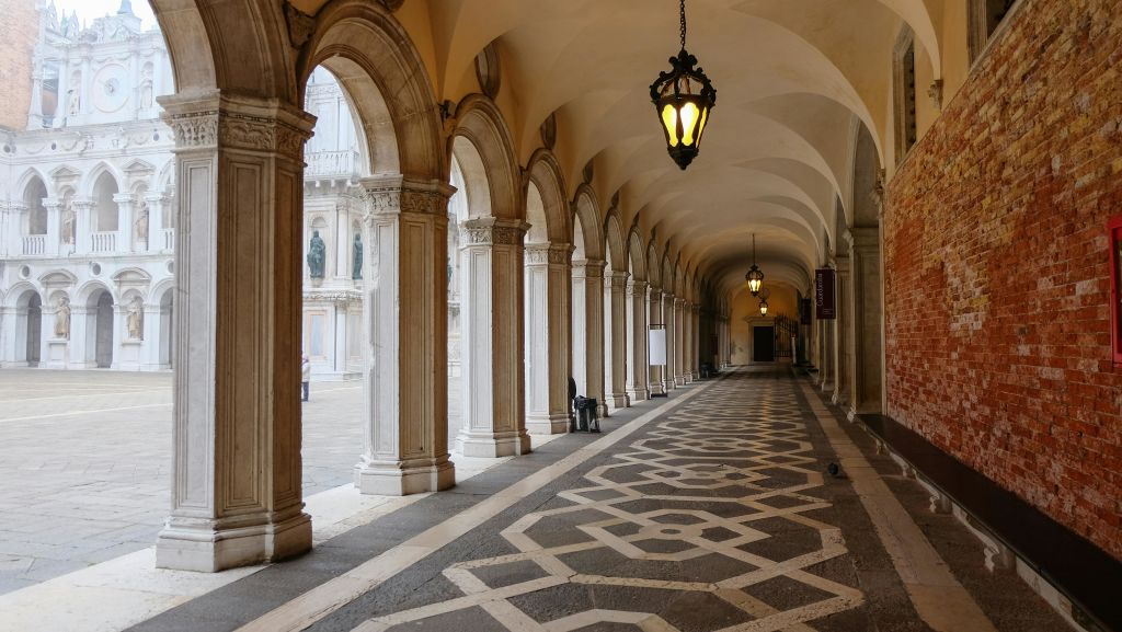 화려한 기둥과 매달린 등불로 덮인 통로로, 무늬가 있는 바닥과 아치형 통로를 통해 탁 트인 안뜰로 연결됩니다.