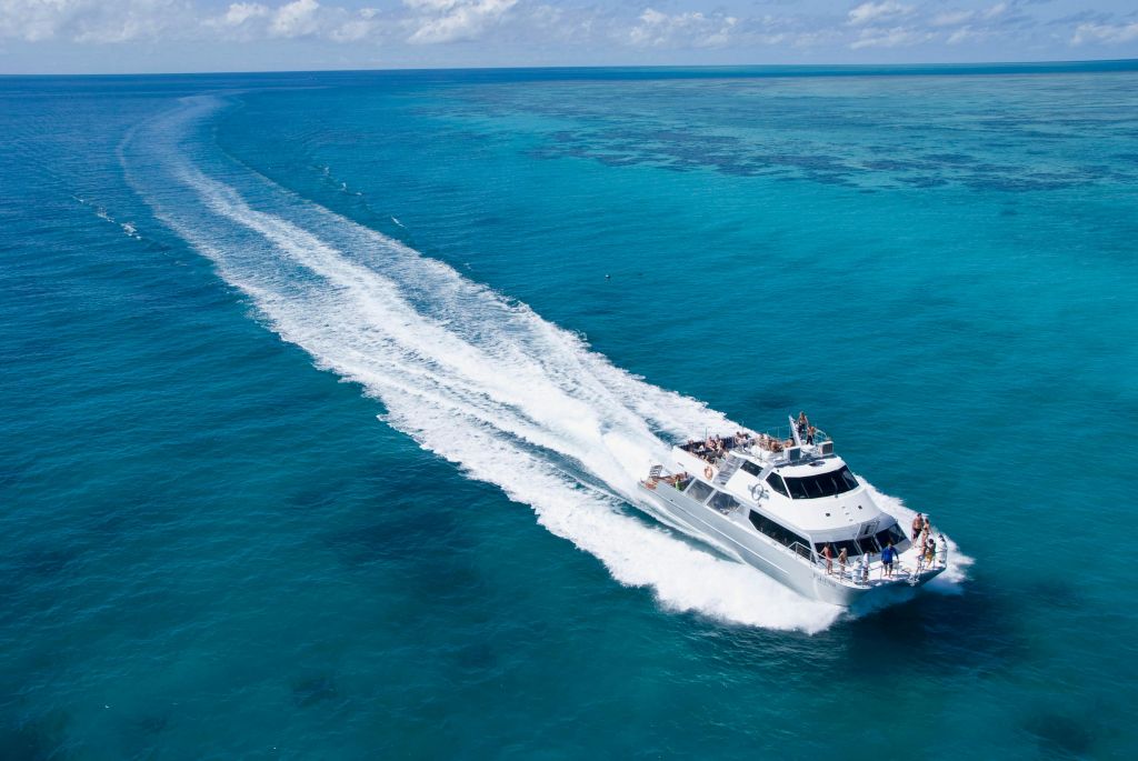 흰색 보트가 부분적으로 흐린 하늘 아래에서 파도의 흔적을 남기며 맑고 푸른 바다를 빠르게 통과합니다.