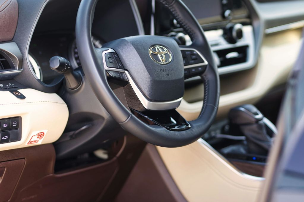 Toyota 로고, 제어 버튼 및 내부 대시보드의 일부가 표시된 자동차 스티어링 휠의 클로즈업.