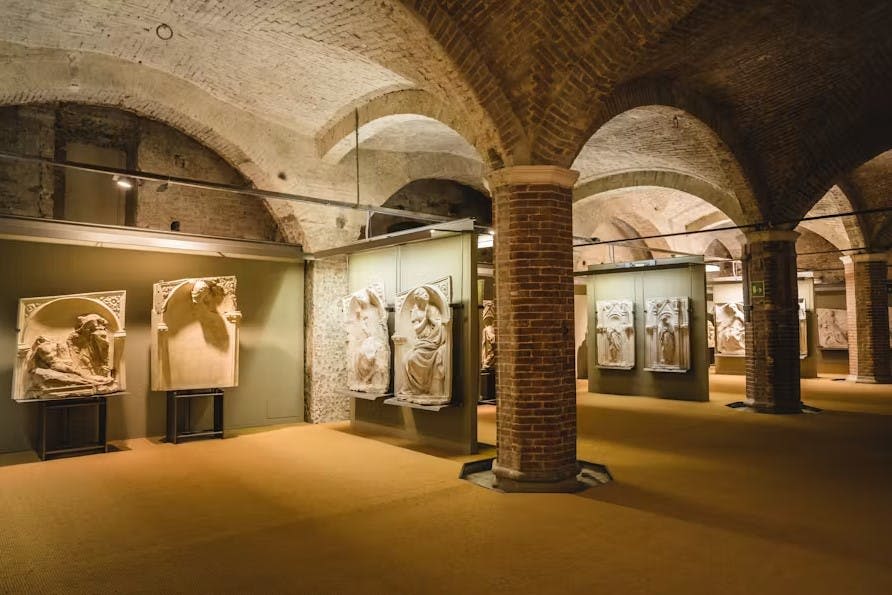 벽돌 아치가 있는 지하 박물관 갤러리는 녹색 벽에 고전적인 석조 조각을 전시합니다.