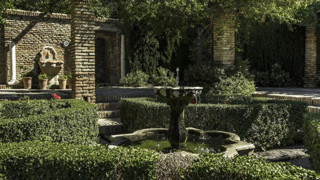 울창한 정원에 깔끔하게 다듬어진 울타리와 벽돌 아치로 둘러싸인 석조 분수.