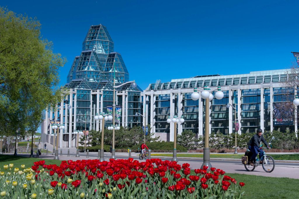 전등 기둥, 자전거 타는 사람, 붉은 튤립으로 둘러싸인 독특한 건축 디자인의 현대적인 유리 건물입니다.