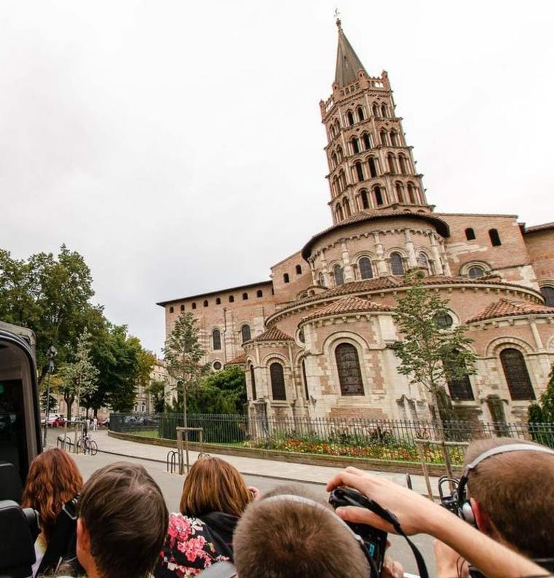 헤드폰을 착용한 한 무리의 사람들이 흐린 하늘을 배경으로 높고 화려한 탑이 있는 유서 깊은 교회를 바라보고 있습니다.