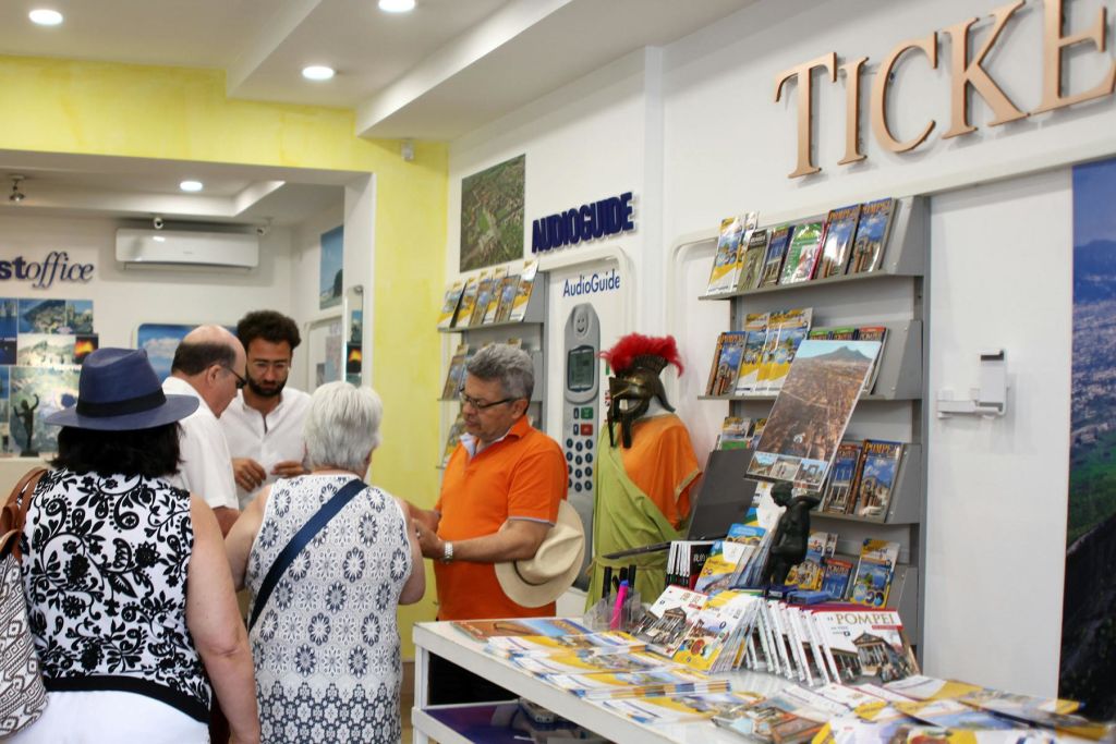 사람들이 관광 안내소 안으로 모여 안내 책자를 보고 직원들과 이야기를 나눕니다.