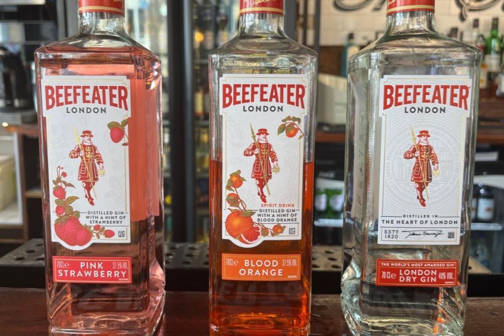 핑크 스트로베리, 블러드 오렌지 및 런던 드라이 품종이 특징인 비피터 진 3병이 선반에 진열되어 있습니다.