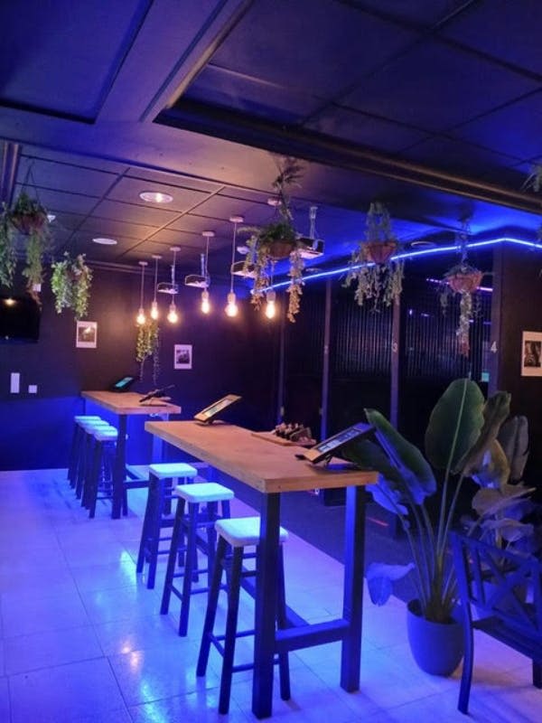 높은 테이블, 스툴, 걸이식물, 파란색 주변 조명이 있는 현대적인 라운지. 천장 전구는 따뜻한 빛을 선사합니다.