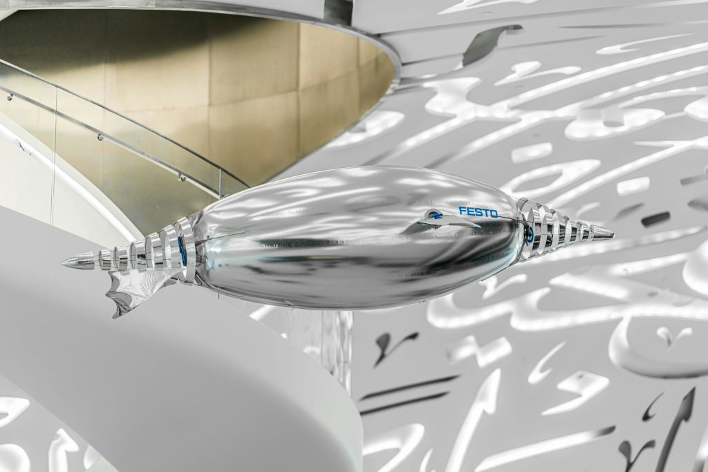 현대적이고 추상적이며 조명이 밝은 실내 환경에 'Festo' 로고가 있는 은색의 간결한 로봇 장치입니다.