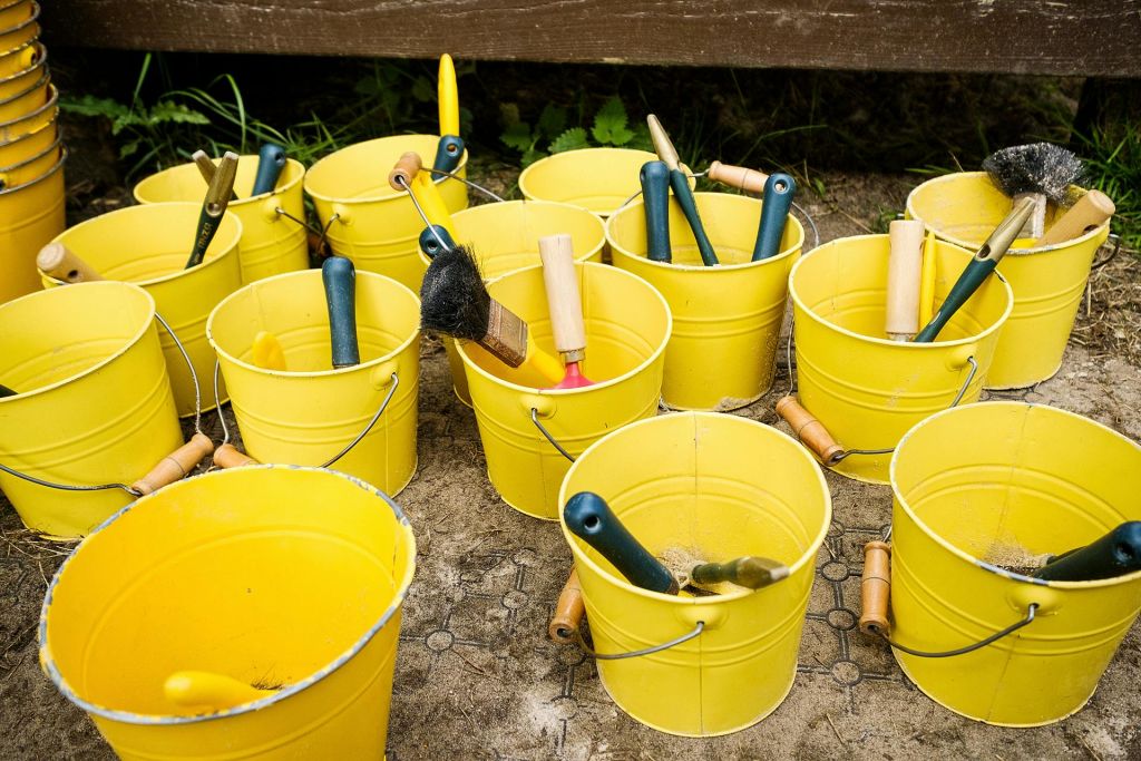 다양한 붓과 도구가 들어 있는 여러 개의 노란색 양동이가 무늬가 있는 타일로 덮인 바닥에 놓여 있습니다.