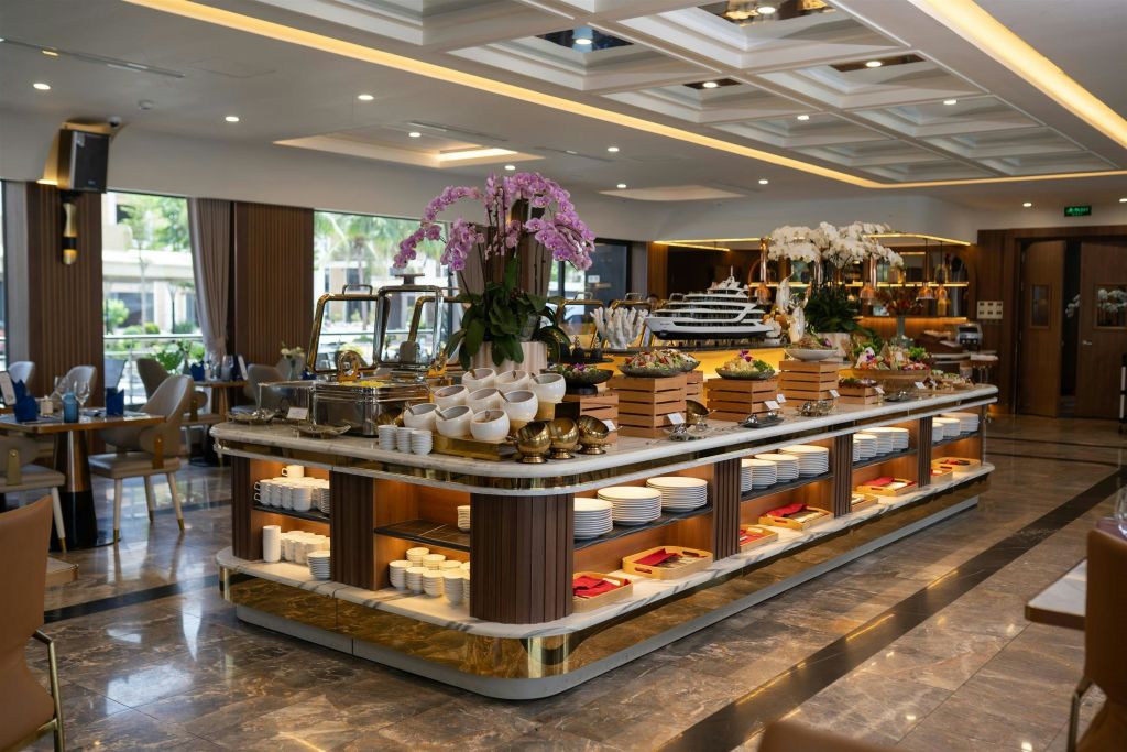 다양한 요리, 접시, 그릇을 갖춘 우아한 뷔페 세트. 넓은 식사 공간에 난초를 포함한 꽃으로 장식되어 있습니다.