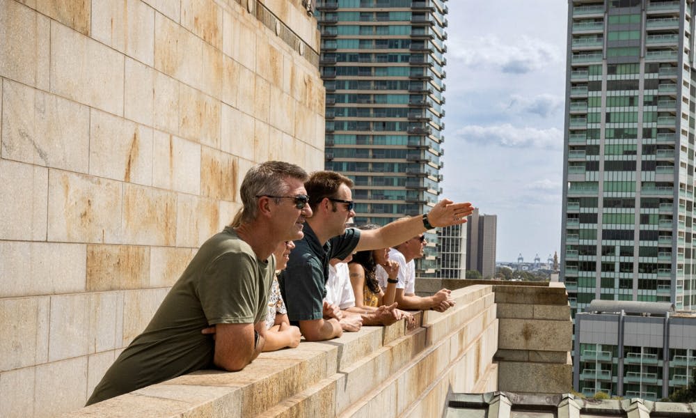 사람들은 옥상 발코니에 서서 도시 풍경과 높은 건물을 배경으로 바깥을 바라보고 있습니다.