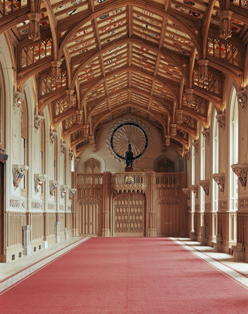 화려한 나무 천장, 아치형 창문, 레드 카펫, 맨 끝에 커다란 장식 바퀴가 있는 웅장한 복도.