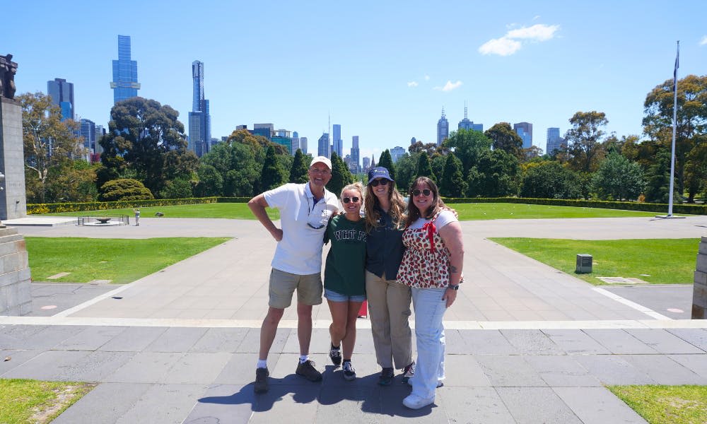 화창한 날, 도시의 스카이라인을 배경으로 공원 앞에서 네 사람이 함께 포즈를 취하고 있습니다.