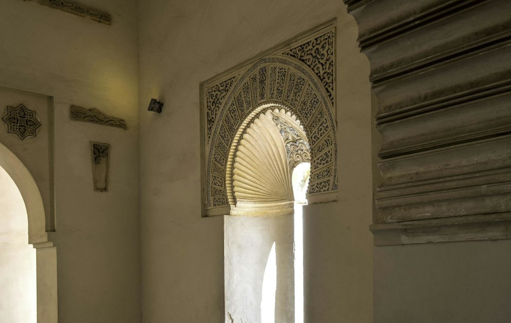 정교한 조각과 선풍기 모양의 건축 디테일이 돋보이는 아치형 창문을 장식하여 미니멀한 공간에 조명을 비춥니다.