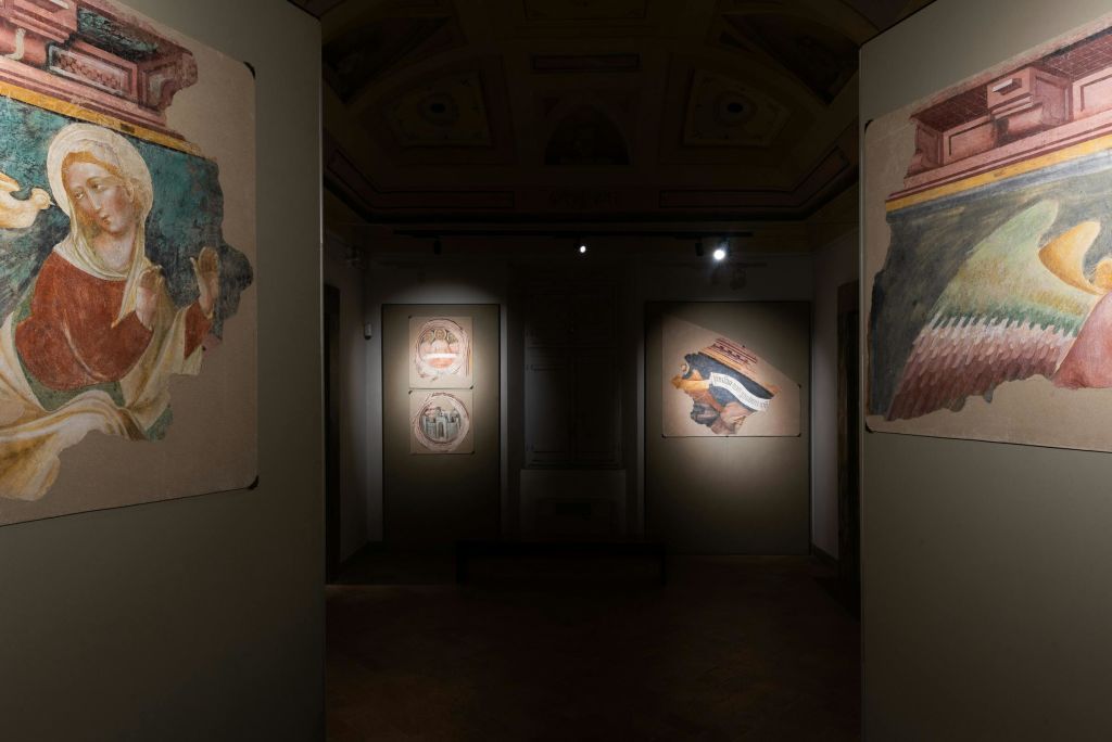 조명이 희미한 갤러리는 벽에 고대 프레스코화를 전시하고, 스포트라이트는 베이지색 배경의 특정 조각을 강조합니다.