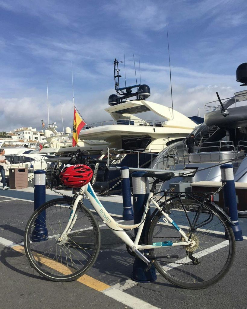 붉은 헬멧을 쓴 자전거가 부분적으로 흐린 하늘 아래 정박지에 있는 요트 근처에 주차되어 있습니다.