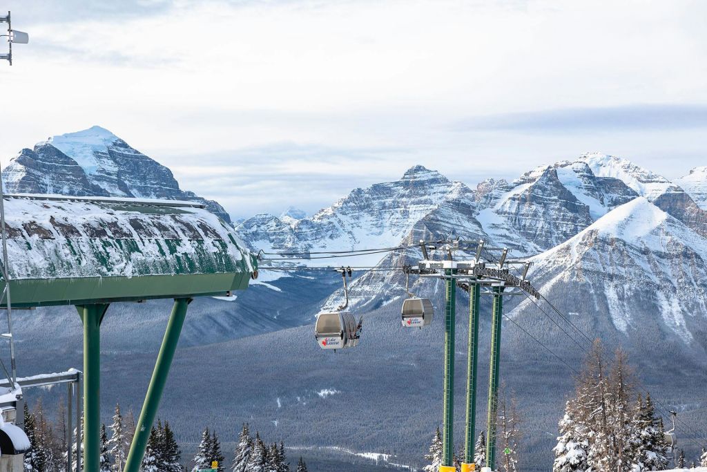 곤돌라를 실은 스키 리프트가 있는 눈 덮인 산으로, 나무로 둘러싸여 있으며 전경에 스키장 구조물이 있습니다.