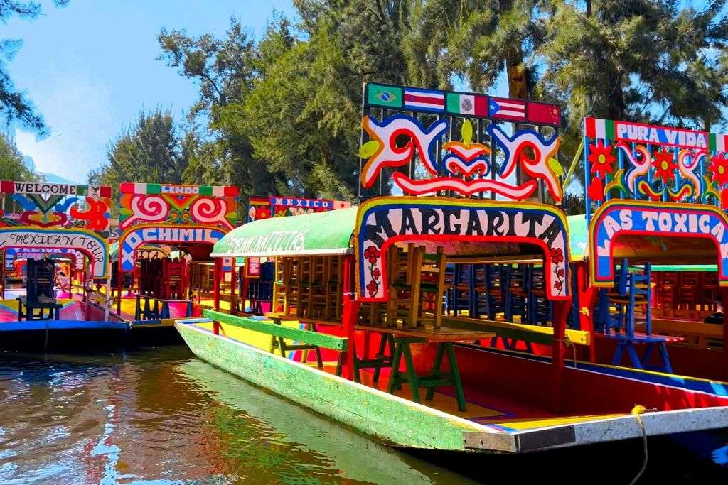 화창한 날 나무 근처에 정박해 있는 '마르가리타' 와 '소치밀코' 라는 이름과 생동감 넘치는 디자인의 화사한 보트.