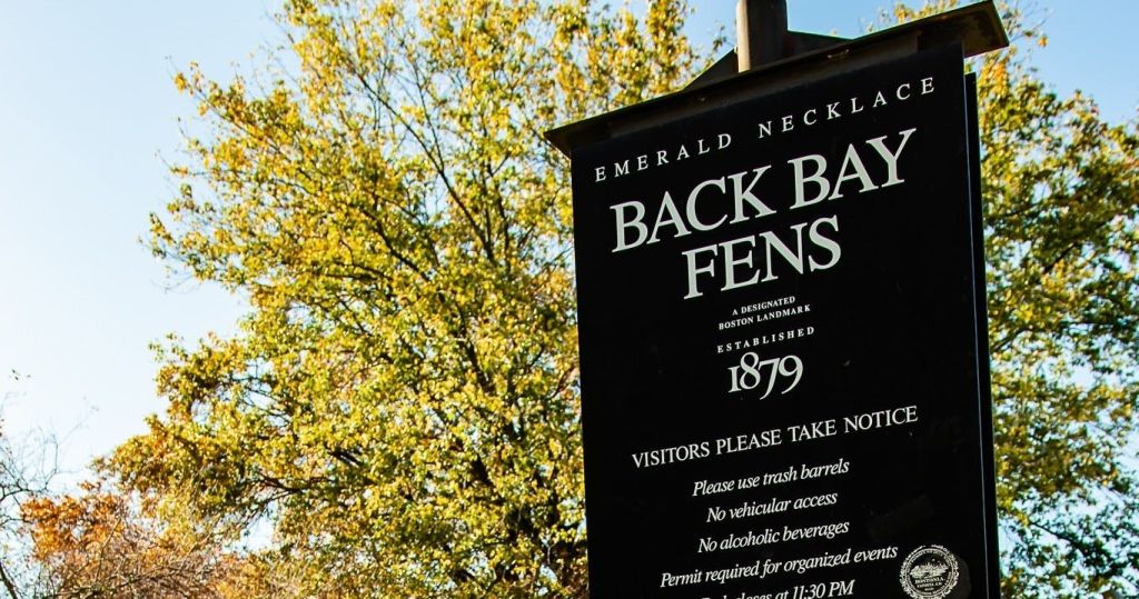 나무와 화창한 하늘을 배경으로 1879년에 세워진 보스턴의 백 베이 펜스 (Back Bay Fens) 표지판입니다.