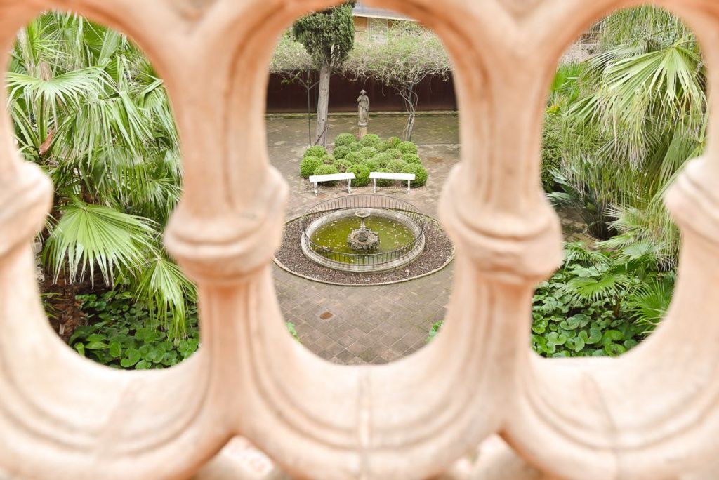 중앙 분수대, 두 개의 흰색 벤치, 울타리, 서 있는 조각상을 배경으로 안뜰의 석조 난간을 내려다보세요.