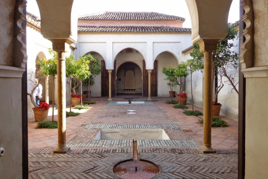 아치형 출입구, 화분에 있는 나무, 무늬 타일로 둘러싸인 중앙 수질 특징이 있는 안뜰.