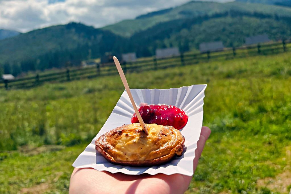 녹색 산과 들판을 배경으로 작은 페이스트리와 빨간 소스가 담긴 트레이에 나무 막대기가 삽입되어 있습니다.