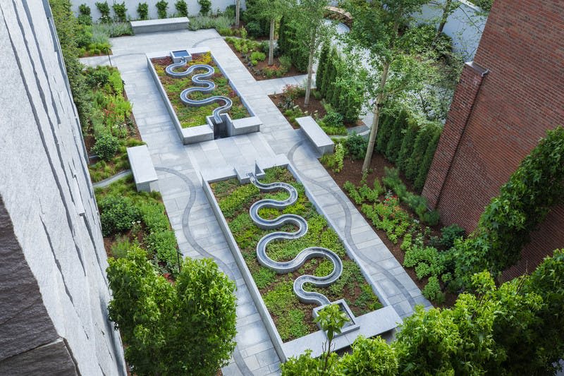 깔끔하게 조경된 녹지와 길로 둘러싸인 곡선형 금속 물길이 특징인 긴 침대 2개가 있는 현대적인 정원.