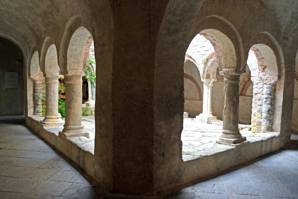 석조 아치와 기둥은 자갈 바닥과 녹지가 배경으로 보이는 부분적인 안뜰을 이룹니다.