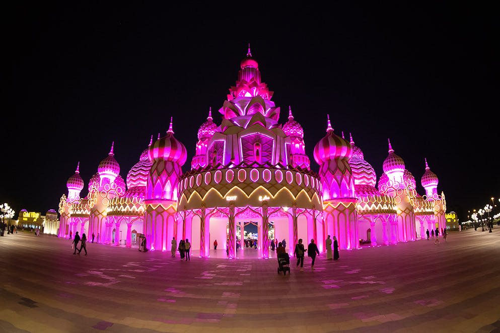 밤에는 분홍색 돔과 첨탑이 있는 화려한 건물에 사람들이 걷고 서 있습니다.